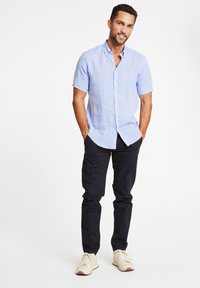 Lichtblauw kortom mouwig button-up shirt in linnenmix, gedragen met donkere chino's en witte sneakers. Kenmerken een casual, ontspannen pasvorm.