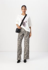 Hvit oversized t-skjorte med grafisk trykk, kombinert med vide bukser i leopardmønster og en liten svart crossover-bag. Svart hæl-sko.