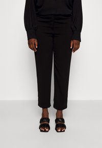 Svarta skräddarsydda byxor med rak skärning och en slät textur, kombinerat med svarta sandaletter med remmar och volangdetaljer.