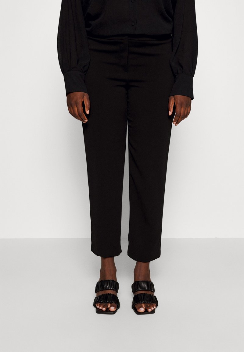 Svarta skräddarsydda byxor med rak skärning och en slät textur, kombinerat med svarta sandaletter med remmar och volangdetaljer.