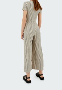 Combinaison rayée en beige et noir avec des manches courtes, une coupe ample et une texture douce. Associée à des sandales noires, affichant un design décontracté.