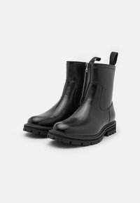 Botas de tobillo de cuero negro con cremallera lateral, suela de goma texturizada, tira de agarre y acabado suave. Diseño voluminoso con un aspecto brillante.