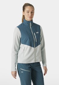 Chaqueta de forro polar con un alto cuello, que presenta una sección superior azul y una sección inferior gris claro. Tiene un bolsillo con cremallera y un logo en el pecho.