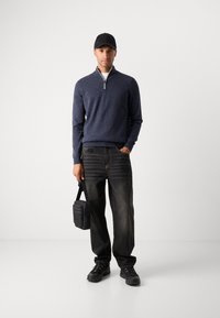 Navy sweater with a half-zip collar over a white shirt, paired with dark jeans and black sneakers. Black crossbody bag.