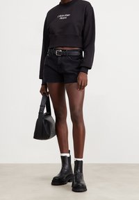 Svart kortärmad sweatshirt med vit logotyp, svarta denimshorts med fransade kanter, svarta ankelboots och en liten svart axelväska.