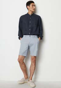 Cămașă albastră cu nasturi, cu guler și buzunar, asortată cu pantaloni scurți în carouri bleu deschis și pantofi bej cu șireturi. Țesătură netedă, croială lejeră.