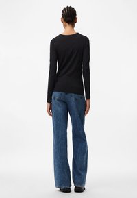 Sort langærmet top parret med brede blå jeans. Toppen har en rund hals; jeansene har en falmet vask og synlige baglommer.