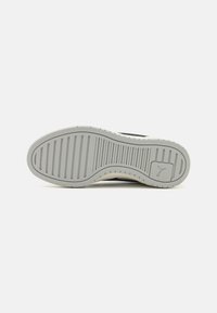 Suola della scarpa in un materiale gommoso grigio chiaro, con una superficie testurizzata e righe orizzontali; dettaglio del logo vicino al tallone.