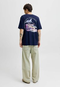 Granatowa koszulka bawełniana z kolorowym nadrukiem na plecach z napisem, w połączeniu z jasnopomarańczowymi spodniami o szerokich nogawkach.