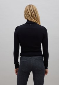 Maglione a collo alto a coste nere con maniche lunghe, abbinato a jeans grigio scuro con tasche posteriori e vestibilità slim.