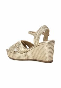 Sandali con zeppa in una texture dorata intrecciata, con cinturini incrociati e un tacco solido. La piattaforma ha un design testurizzato.