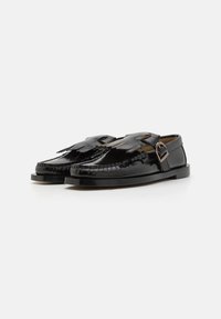 Schwarze Lederschuhe mit einem einzigartigen Fransen-Design auf der Vorderseite, Schnallen-Detail und flacher Sohle. Glatte Textur mit genähten Akzenten.