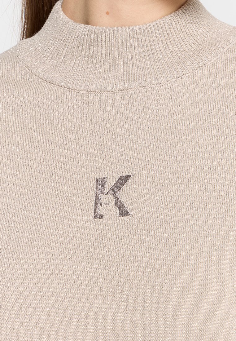 Maglione beige lavorato a maglia con colletto a mock neck a coste e una lettera "K" grigia ricamata sul petto.