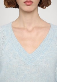 Jasnoniebieski sweter w serek wykonany z miękkiego, puszystego materiału, z teksturowanym wzorem dzianiny oraz aksamitem w okolicy ramion.