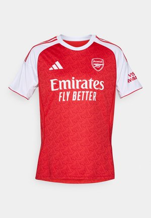 Rød fotballtrøye med hvite detaljer, som har et geometrisk mønster, rund hals og Arsenal-logoet, samt "Emirates Fly Better" branding.