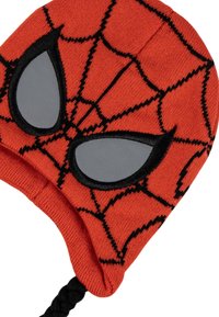 Cappello lavorato a maglia rosso con motivo a ragnatela nera, dotato di occhi di ragno grigi. Include una fascia intrecciata sotto il mento per una vestibilità sicura.