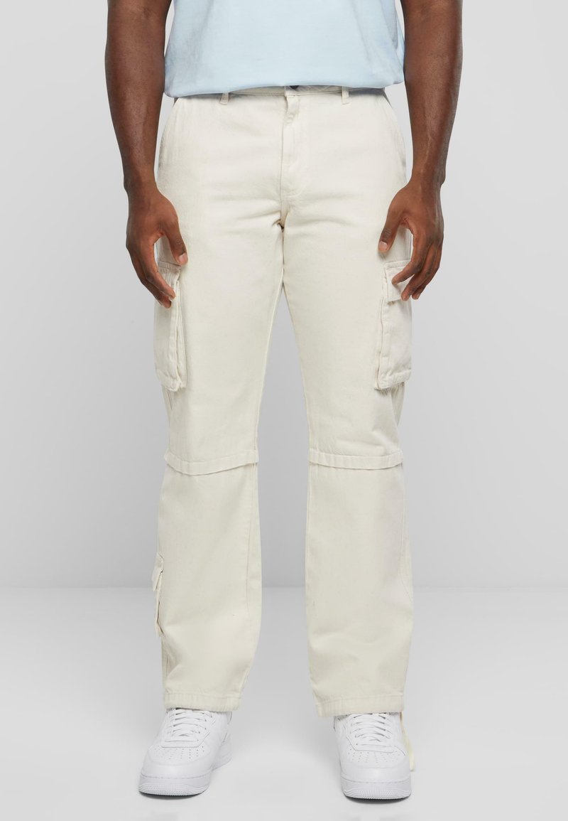 Pantalons cargo beiges avec plusieurs poches latérales, jambes droites et coupe décontractée, associés à des baskets blanches. Fabriqués en tissu en coton durable.