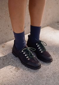 Černé semišové boty se zelenými tkaničkami a stříbrnými očky, s texturovanou gumovou podrážkou. Nosené s námořnickými pruhovanými ponožkami.