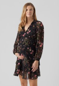 Vestido de maternidad negro con estampado floral, de manga larga transparente, dobladillo con volantes y escote en V. Presenta patrones florales multicolores en una tela suave.
