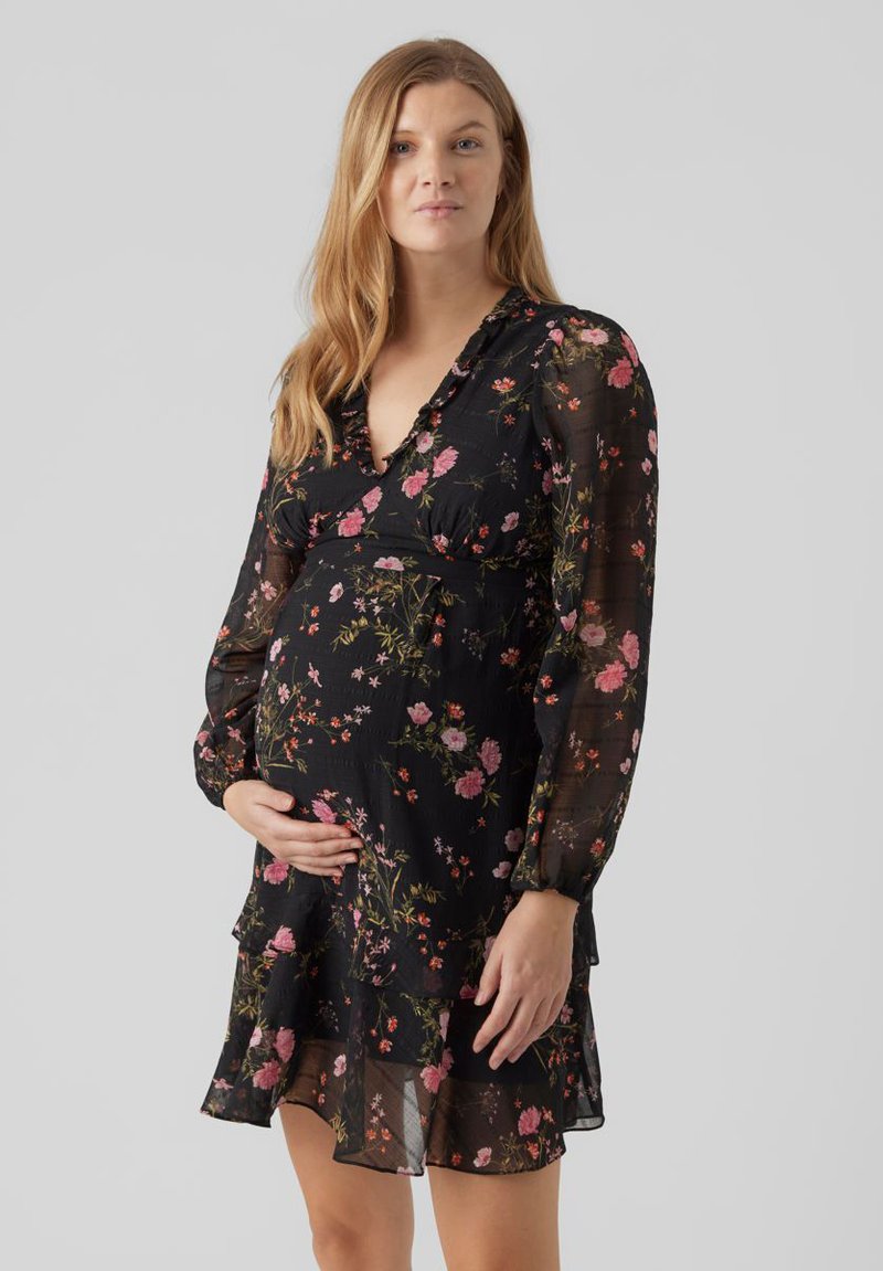 Vestido de maternidad negro con estampado floral, de manga larga transparente, dobladillo con volantes y escote en V. Presenta patrones florales multicolores en una tela suave.