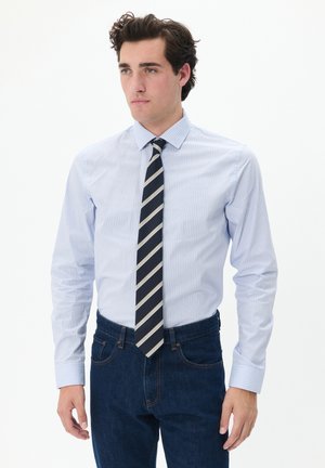 Hellblau gestreiftes Hemd mit Kragen und langen Ärmeln, dazu eine marineblaue Krawatte mit weißen und grauen diagonalen Streifen, kombiniert mit dunkelblauen Jeans.