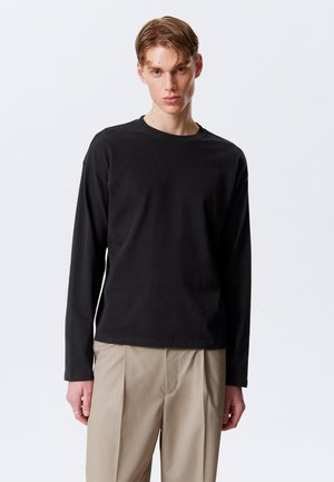 Black long-sleeve t-shirt made of cotton, featuring a crew neck and a relaxed fit. The fabric appears smooth with no patterns or accents.