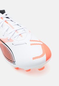 White soccer cleat featuring a textured material, orange accents, and a sleek design with a black stripe and patterned details.