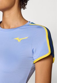 Top atlético azul claro con acentos amarillos y azules, de manga corta y diseño ajustado. Incluye un logo amarillo en el pecho.