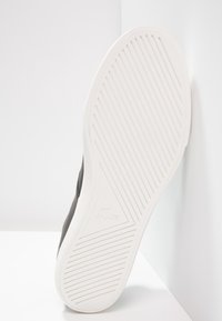 Sole of a sneaker featuring a white rubber base with horizontal and diagonal grooves, accented by a subtle logo. Upper is dark gray.