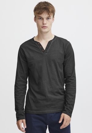 Camisa negra de manga larga hecha de algodón, con escote en forma de V, tres botones marrones en el cuello y una textura suave.