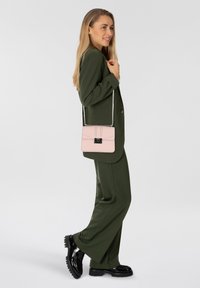 Completo su misura verde con pantaloni a gamba larga e giacca aderente. Borsa a tracolla rosa con tracolla a catena argentata e dettagli neri. Scarpe nere in vernice.