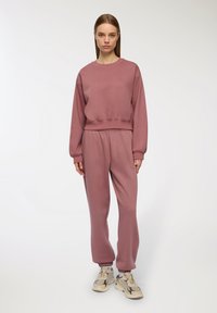 Felpa in cotone rosa con design cropped e polsini a coste, abbinata a pantaloni jogger coordinati con vita elastica e caviglie affusolate.