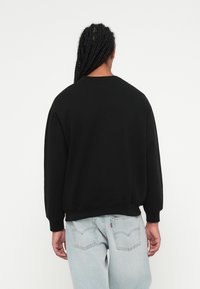 Svart hettegenser med rund hals, ribbestrikkede mansjetter og linning, paret med lysvaskede denimjeans med baklommer og logomerke.