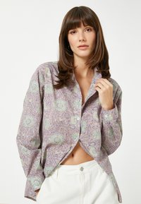 Paarse blouse met bloemenpatroon, voorzien van knopen en lange mouwen, gecombineerd met witte hoge taille broeken. Zacht materiaal met een relaxte pasvorm.
