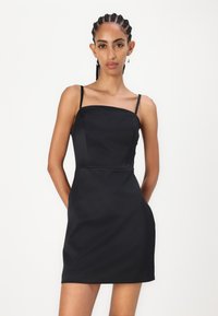 Robe noire sans manches avec un décolleté carrée, corsage ajusté et silhouette droite, fabriquée en tissu lisse. Comprend des bretelles fines.