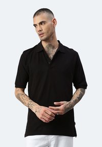 Polo shirt nero a maniche corte con colletto, dotato di bottoni e fondo con spacco laterale. Tessuto dalla consistenza liscia, design aderente.