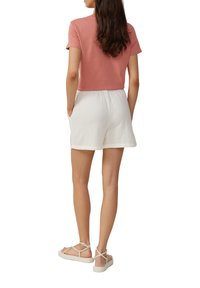 T-shirt rose coupé associé à un short texturé blanc. La tenue présente une coupe décontractée et un design simple. Les chaussures sont des sandales de couleur claire.