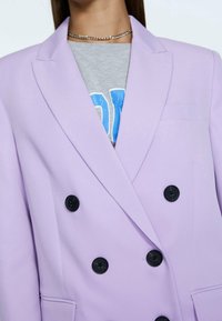 Levandulový dvouřadý blazer vyrobený z hladké látky, s černými knoflíky, klopovými límci a kapsou na hrudi.