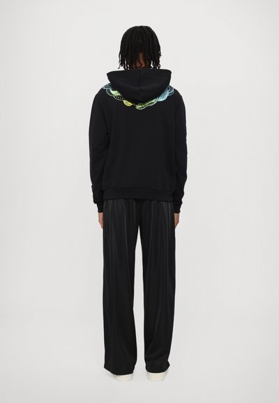 Felpa nera con un design grafico colorato sulla schiena, abbinata a pantaloni neri larghi e scarpe con suola bianca.