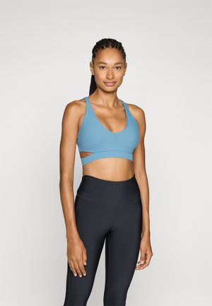 Reggiseno sportivo azzurro chiaro con scollatura a V profonda, dettaglio a taglio e texture a coste, abbinato a leggings neri a vita alta.