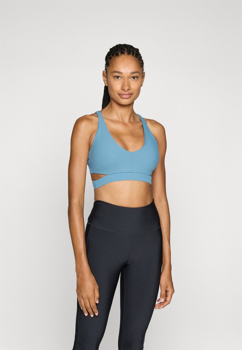 Reggiseno sportivo azzurro chiaro con scollatura a V profonda, dettaglio a taglio e texture a coste, abbinato a leggings neri a vita alta.