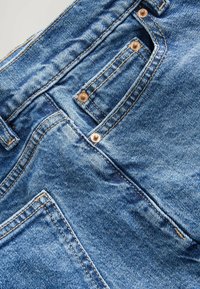 Modré džíny z denimu s texturovaným povrchem, měděnými nýty a standardním rozložením kapes se viditelnými švy.