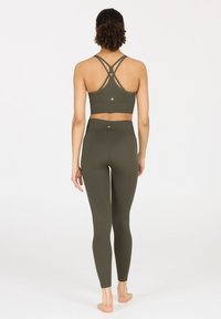 Olivengrünes, kurzes Sport-BH mit überkreuzten Trägern und passenden hochtaillierten Leggings, die über eine gerippte Textur und minimalistische Hardware-Details verfügen.