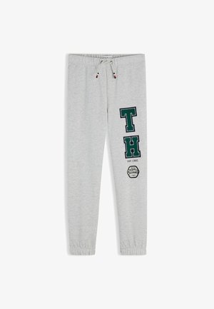 Hellgraue Jogginghose mit elastischen Bündchen, Kordelzug in der Taille und grünen Buchstaben "T" und "H" mit dem Text "EST 1985" und einem runden Logo am Bein.