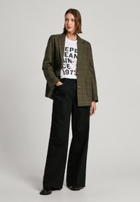 Blazer oversize a quadri marroni sopra una T-shirt bianca con grafica, abbinato a pantaloni neri a vita alta e gamba larga e scarpe nere.