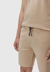 Beige tank top and matching shorts made from textured fabric, featuring an elastic waistband with brown drawstring and metal aglets.