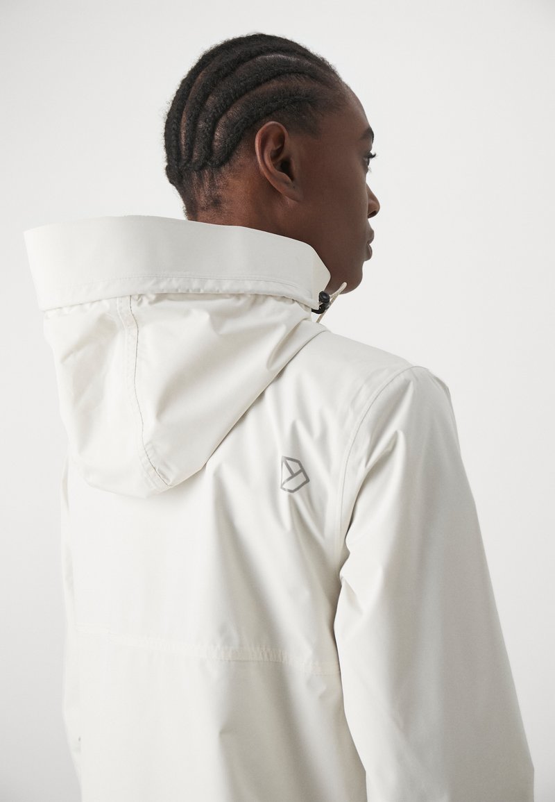 Weiße wasserdichte Jacke mit Kapuze, versehen mit einem silbernen Logo auf der Rückseite. Glatte Textur und minimalistisches Design. Verstellbare Kapuze mit Kordelzug.