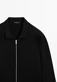 Sort strikket zip-up trøje med krave og sølvlynlås, mærket Massimo Dutti, præsenteret på en hvid baggrund.