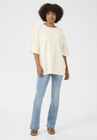 Krämfärgad oversize t-shirt med korta ärmar, tillsammans med ljusblå utsvängda jeans och bruna klacksandaler; mjuk textur, avslappnad passform.