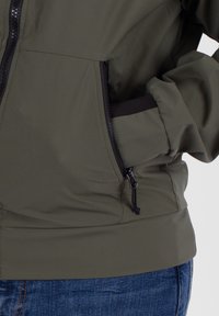 Olivgrüne Jacke mit glatter Textur, mit Reißverschlusstasche und verstellbarem Saum. Verfügt über einen schwarzen Reißverschluss und Akzente in Schwarz.